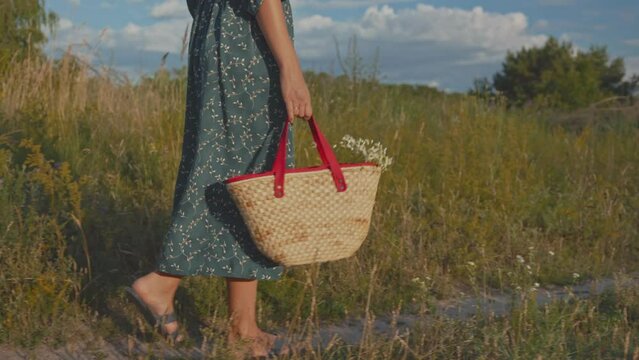 Rural village woman in flower pattern summer dress walking with straw basket or straw bag with daisies flowers