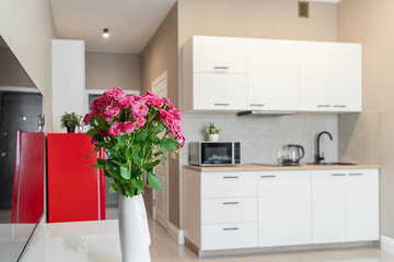 stylish interior of apartment with modern kitchen in white. kitchen design with appliances, microwave, red refrigerator, stove. pink roses near TV 