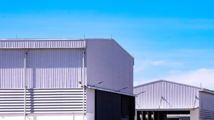 Fototapeta premium White aluminium corrugated steel wall of warehouse building with workshop inside of factory area against blue sky background, perspective side view with copy space 