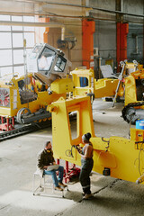 Vertical high angle view wide shot of biracial young man and woman working together at bulldozer production factory, copy space