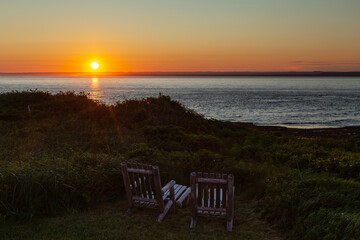 Wooden armchairs set on cliff with beautiful sunset over the St. Lawrence Gulf at the Île aux Perroquets (Parrots Island) in the Mingan Archipelago National Park Reserve, Quebec, Canada