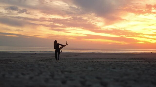 Wide Shot of Female Surfer Walking on Beach with Surfboard at Sunset in Costa da Caparica, Portugal