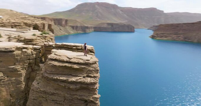 Man Over Towering Lakeside Cliffs Of Band-e Amir National Park In Afghanistan. Aerial Orbiting Shot
