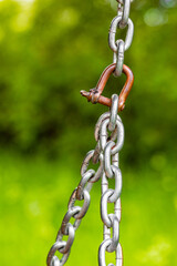 Obraz premium metal chain on a background of green foliage. fragment of an old metal chain. metal chain mount. reliable metal fastening. vertical photo