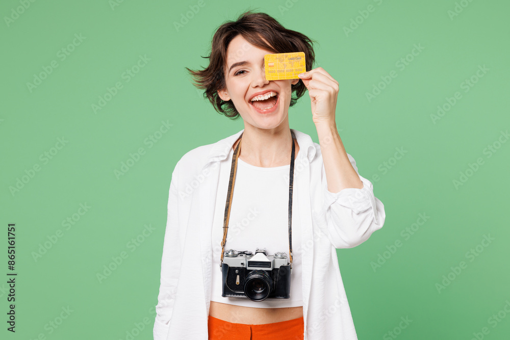 Wall mural Traveler happy rich woman wear casual clothes hold cover eye with credit bank card isolated on plain green background. Tourist travel abroad in free spare time rest getaway. Air flight trip concept.