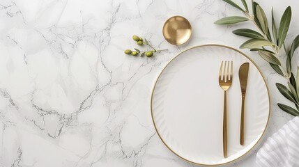 A white marble tabletop with a white plate, gold fork, gold knife, and gold spoon. An olive branch with green leaves extends from the left side of the frame