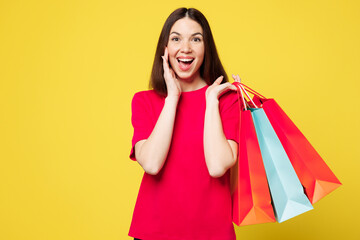 Young woman wears pink casual clothes hold paper package bags after shopping sharing hot news about sales scream, hand near mouth isolated on plain yellow background Black Friday sale buy day concept