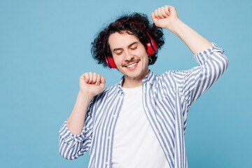 Naklejka premium Young smiling fun man wear shirt white t-shirt casual clothes listen to music in headphones raise up hands dance isolated on plain pastel light blue cyan background studio portrait Lifestyle concept