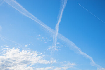 crossing contrails of two airplanes. water vapor and exhaust gases appear as ice clouds in the blue...