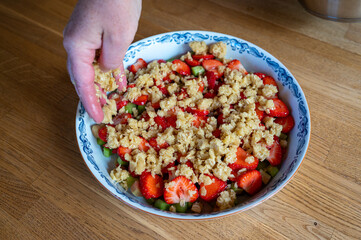 woman pouring crumb dough over fruits making a pie
