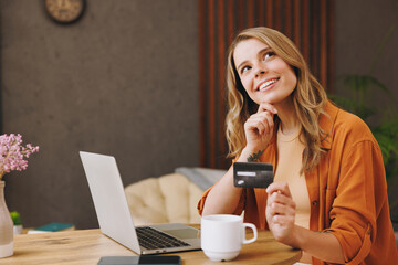 Young woman wear shirt use laptop pc computer hold credit bank card shopping online sits alone at table in coffee shop cafe relax rest at restaurant indoor. Freelance mobile office business concept.