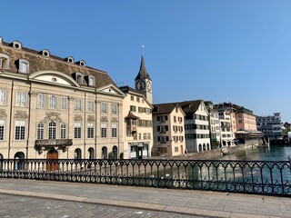 Obraz premium Panorama auf die Altstadt Zürich am Fluss Limmat, mit Helmhaus, Wasserkirche, Altstadthäuser von der Münsterbrücke aus. Kirchturm, St. Peter, Kirche im Hintergrund, Wühre am Flussufer
