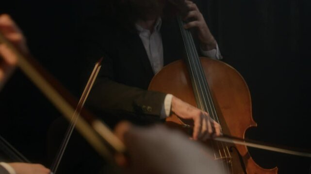 Cropped shot of talented string orchestra playing musical instruments on black background during concert