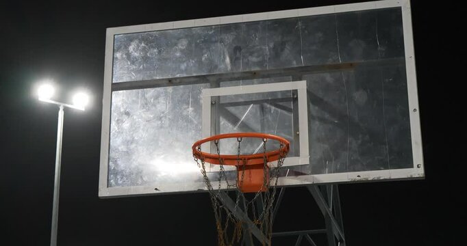 Red basketball rim. Basketball backboard and hoop. Sports ground is illuminated by a lantern in evening. Cinema 4K 60fps tilt view video