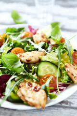 Salad with Chicken Breast, Cherry Tomatoes, Cucumber, Rocket and fresh Basil. Bright wooden background. Close up.
