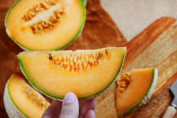 Ripe yellow melon cut into slices on a wooden board next to a knife and linen napkin