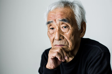 Stunning elderly Japanese man with a thoughtful expression, looking at the camera, isolated on white background.