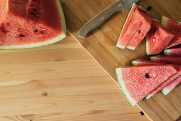Cutting into triangular pieces watermelon on a wooden cutting board.