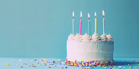 Delicious white birthday cake with five lit candles and colorful sprinkles on a light blue...