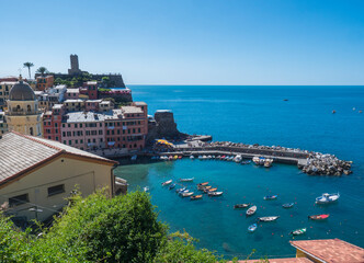 Naklejka premium Picturesque view of Vernazza, with colorful houses, harbor, fishing boats, Vernazza Castle and clear blue sky. Typical traditional village in National park Cinque Terre, Vernazza,, Liguria, Italy