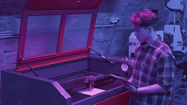 Man watches printing process. Media. Young developer monitors printer operation from tablet. Modern development of robotic printer in laboratory