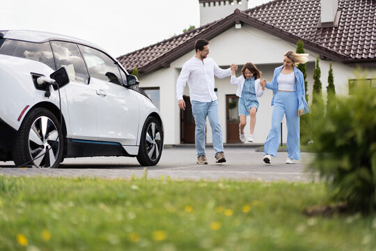 Happy Family Enjoying Time Together Near Electric Car Outside Modern Home