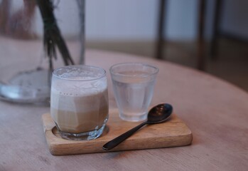 Dirty latte with a glass of water and spoon on a wooden tray.