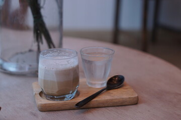 Dirty latte with a glass of water and spoon on a wooden tray.
