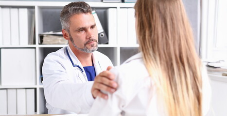 Fototapeta premium Friendly male doctor hold patient shoulder in office during reception. Examination result positive test calm down promise and cheer up grief and suffer treatment condolence ethics concept