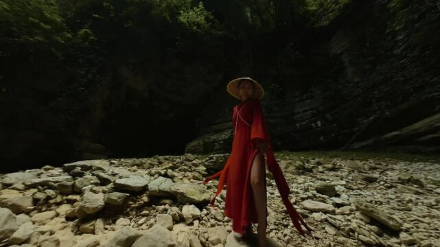 An Asian girl in a beautiful red kimono and a Vietnamese triangular hat is dancing sexually in nature in a rocky canyon
