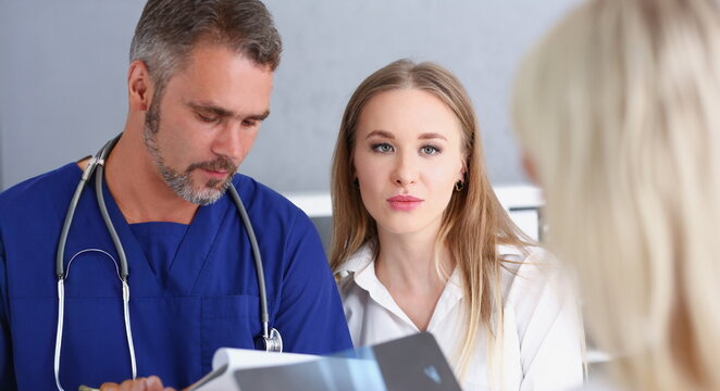 Smiling handsome doctor communicate with patient holding silver pen and showing pad. Physical agreement signature disease prevention interpreter translator prescribe remedy healthy lifestyle