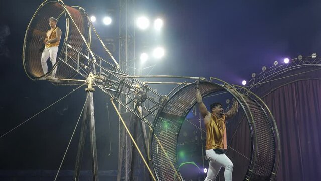 Portrait of brave acrobats on the rotating wheel of death under the dome of the circus. A huge spinning wheel with acrobats inside. Circus performance.