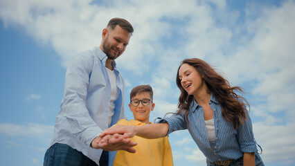 Obraz premium Low angle happy friendly Caucasian family parents mother father little boy son kid child hands stack team celebrate teamwork gesture enjoying together outside nature friendship unity childcare support
