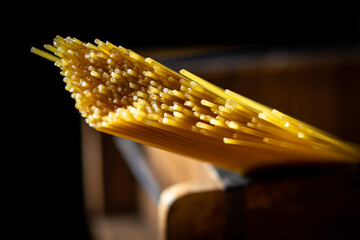 Close-up of uncooked spaghetti clamped in a wooden vise against a dark background. The noodles are neatly aligned, capturing the texture and color of the dried spaghetti. 