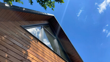 Wooden facade of a house with a plastic gray triangular window, aframe.