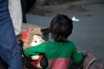 A poor girl with her doll in a street.