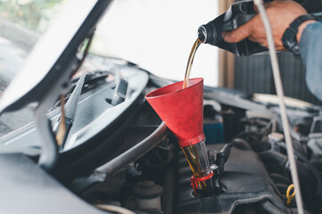Close-up of hand pouring engine oil into a red funnel under the car hood during a vehicle...