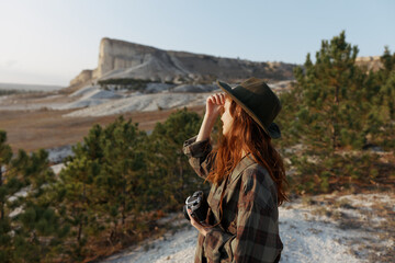 Stylish woman in plaid shirt and hat standing proudly in front of majestic mountain landscape