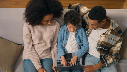Top view African American family married couple teaching little boy child son kid offspring typing...