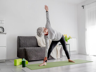 Retired Woman Practices Yoga, Doing Bends At Home In Living Room