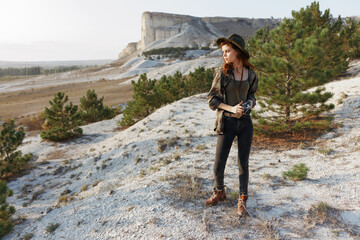 Serene woman in widebrimmed hat standing confidently on hilltop with lush green trees in background