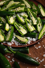 Cutaway green hot jalapeno pepper. Mexican green peppers sprinkled with salt on plate. Peeled fresh pepper. Pepper seeds. Pod halves. Mexican snack. Wooden background. Top view. Soft focus.