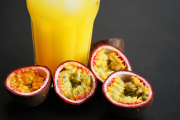 Passion fruits cut in half next to a glass of juice with ice on a dark background