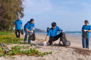 Fototapeta premium Plastic pollution and environmental problem concept. Happy asian diverse group of volunteers with garbage bags wearing blue t-shirt and cleaning plastic on the beach. Volunteers collecting trash.