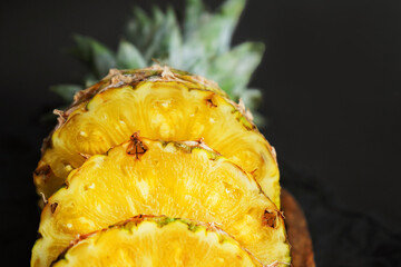 Ripe pineapple cut into slices on a wooden tray on a dark background