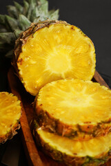 Ripe pineapple cut into slices on a wooden tray on a dark background