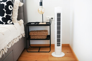 White tower fan next to a bed and bedside table with a lamp in a modern bright interior