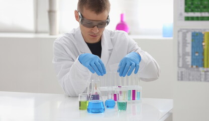 Fototapeta premium A male chemist holds test tube of glass in his hand overflows a liquid solution of potassium permanganate conducts an analysis reaction takes various versions of reagents using chemical manufacturing.