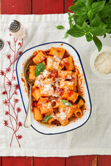 Pasta Rigatoni with parmesan cheese, tomato passata sauce and basil in retro plate on old wooden red  rustic table background. Traditional Italian pasta recipe. Cover or article. Top view.