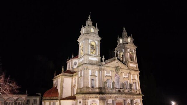 Close-up night drone shot from the base of Sanctuary of Bom Jesus do Monte in Braga, Portugal, slowly rising to reveal the illuminated fa&ccedil;ade and towers